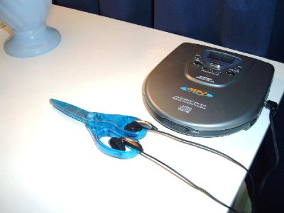 Ohrknöpfe eines mobilen CD-Spielers ruhen in den Griffen einer blauen Kinderschere